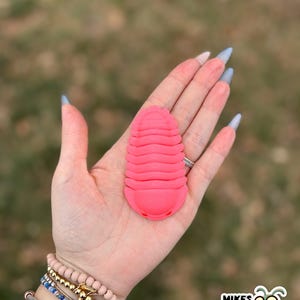 May include: A bright pink, 3D-printed trilobite model. The model is held in a hand with long, pointed nails. The image includes a logo for "Mikes Bug Box" in the bottom right corner.