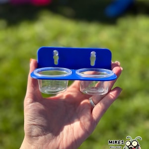 May include: A blue plastic bug box with two clear plastic cups. The bug box is held in a hand against a green grassy background. The text "MIKES BUG BOX" is in the lower right corner with a cartoon bug.