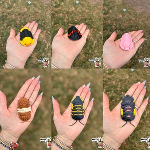 May include: A collection of colorful, stylized trilobite figurines in various colors, including yellow, black, pink, and brown. Each figurine is held in a hand, showcasing the detailed design and vibrant hues. The figurines have a cartoonish appearance.