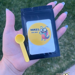 May include: A black resealable pouch with a white label that says "Mikes Bug Box" and features a cartoon bug with glasses. A yellow plastic scoop is in front of the pouch.
