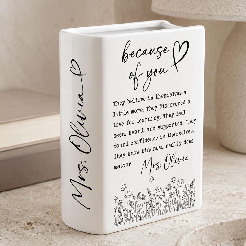 Puede incluir: Un florero rectangular de cer&aacute;mica blanca con texto en negro que dice because of you, seguido de un p&aacute;rrafo sobre la confianza y la amabilidad. El lateral est&aacute; personalizado con Mrs. Olivia y la base muestra un dise&ntilde;o floral de l&iacute;neas negras.