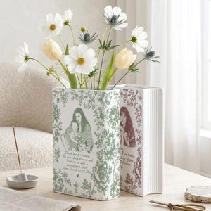 May include: Two rectangular white ceramic vases shaped like books, decorated with green and maroon floral patterns and custom portraits. The front vase features a green illustration of a person holding a baby with text below, while the second vase displays a maroon portrait and script text.
