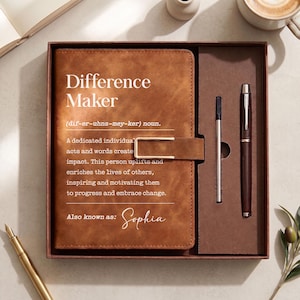 May include: A tan leather-look journal with a gold-tone metal clasp and the printed text Difference Maker, a definition, and the name Sophia, presented in a rectangular box alongside a dark brown pen and a thin metal refill cartridge.