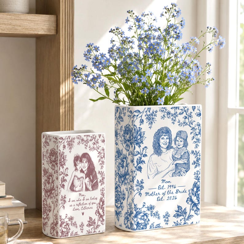 May include: Two rectangular ceramic vases featuring blue and maroon floral patterns. The larger vase displays a blue illustration of two people with text reading Mom Est. 1996 Mother of the Bride Est. 2026. The smaller vase has a maroon illustration.