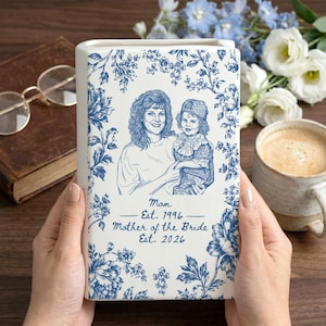 May include: A white rectangular ceramic vase featuring a blue floral pattern and a line art illustration of a woman and a child. The text reads: Mom Est. 1996 Mother of the Bride Est. 2026. The design is printed on the front of the vertical ceramic piece.