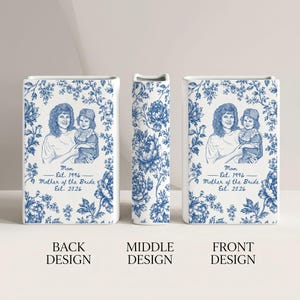 May include: A rectangular white ceramic vase featuring a blue floral pattern. The front and back display a line drawing of a person holding a child with the text: Mom Est. 1996, Mother of the Bride Est. 2026. The middle section shows a floral design.