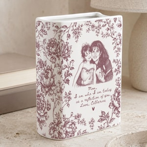 May include: A rectangular white ceramic vase featuring a dark pink floral pattern. The front displays a sketch of two people and the text: Mom, I am who I am today as a reflection of you. Love, Catherine, with a small heart symbol below the text.