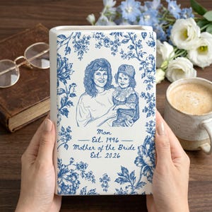 May include: A white rectangular ceramic vase featuring a blue floral pattern and a line art illustration of a woman and a child. The text reads: Mom Est. 1996 Mother of the Bride Est. 2026. The design is printed on the front of the vertical ceramic piece.