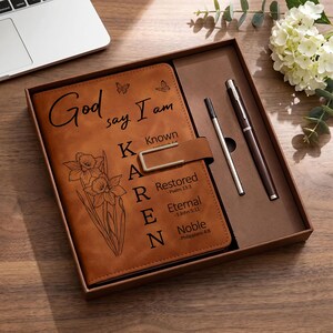 May include: A brown leather-like journal set in a gift box featuring a metal clasp, a matching pen, and a refill. The cover is engraved with the text God say I am, the name KAREN, and floral illustrations of daffodils and butterflies.