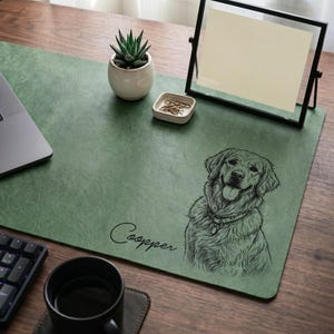 May include: Green desk mat with a detailed illustration of a Golden Retriever dog and the name "Cooper" in script. A small succulent plant in a white pot, a black framed photo, and a cup of coffee are also on the desk.