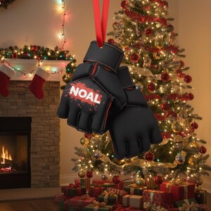 May include: Black and red boxing glove ornament with the name "NOAL" in white. The ornament hangs from a red ribbon against a Christmas tree background. The tree is decorated with lights and ornaments. Presents are under the tree.