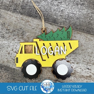 Può includere: Un camioncino ribaltabile di legno giallo con un albero di Natale verde nella cassa. Il camioncino ha ruote nere e il nome "LOGAN" scritto sul lato. L'anno "2025" è scritto sul retro del camioncino.