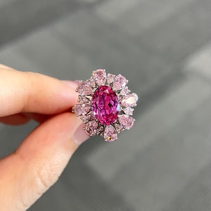 Może przedstawiać: Pierścionek z owalnym różowym kamieniem szlachetnym i halo mniejszych różowych kamieni szlachetnych w kształcie gruszki.