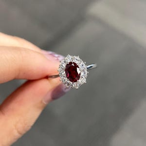 Op de afbeelding: Een zilveren ring met een grote ovale robijn omringd door een halo van kleinere diamanten.