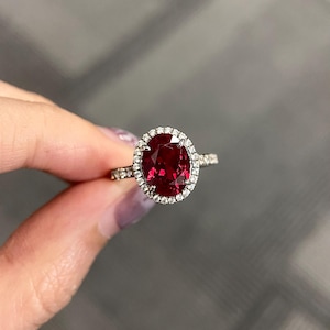 May include: A red oval gemstone ring with a diamond halo setting.