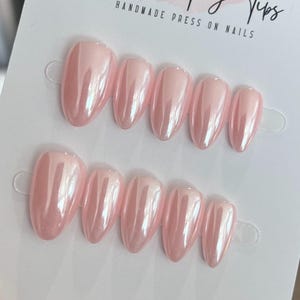 Pode incluir: Dois conjuntos de unhas postiças feitas à mão em tom rosa perolado. As unhas têm formato oval e acabamento brilhante. O texto "HANDMADE PRESS ON NAILS" é visível no topo.