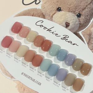 May include: A nail polish color chart with a variety of shades, including pinks, peaches, and blues. The card is labeled "Cookie Bear" and features the text "@YOGURTNAIL.CO.KR". The nail polish colors are arranged in rows and columns.