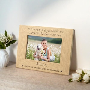 May include: A light-coloured wooden picture frame displaying a photograph of a woman and a dog. The frame is inscribed with the words "YOU WERE OUR favourite HELLO...AND OUR hardest GOODBYE" and "BELLA FOREVER LOVED NEVER FORGOTTEN".
