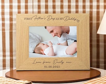 May include: A light-colored wooden picture frame with a photo of a father and baby. The frame has the text "FIRST Father's Day as my Daddy" and "Love from Emily" with the date 01.26.2025.
