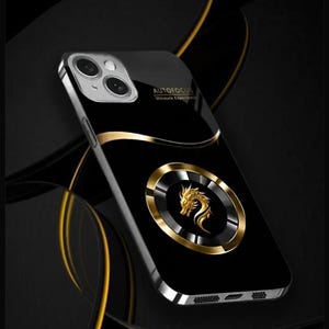 Puede incluir: Una funda de teléfono negra con un anillo dorado y un diseño de dragón dorado. La funda tiene el texto "AUTOFOCUS Ultimate Experience" en la parte posterior.
