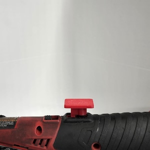 May include: A red and black power tool with a red button on the top. The tool has a black rubber grip and the text "RATCHET" and "WARNING" on the side.