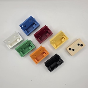 May include: An assortment of small, rectangular, hinged plastic boxes in various colors, including white, blue, red, yellow, green, orange, black, and beige. Each box has a rectangular opening and several small holes.