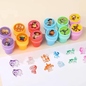 以下が含まれることがあります： 様々なキャラクターが描かれた、カラフルなプラスチック製のスタンプのコレクション。スタンプは紫、黄、赤、青、緑の色合いです。スタンプされた画像が白い面に表示されています。これらのスタンプは、子供向けの工作や教育活動に使用される可能性があります。