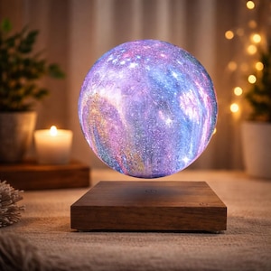 May include: A spherical lamp featuring a vibrant galaxy print with shades of purple, blue, and pink, suspended above a square wooden base. The surface of the sphere displays a detailed nebula pattern with small white star-like specks throughout.