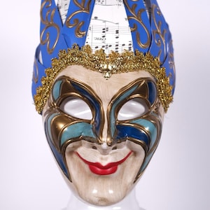 May include: A blue and gold masquerade mask with a jester's hat. The hat is made of paper and has gold trim. The mask has a smiling face with a red mouth.