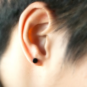Puede incluir: Primer plano de la oreja de una persona con un pequeño pendiente de botón negro.