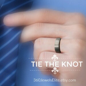 May include: A man's hand wearing a dark gray wedding band. The hand is holding a blue and white striped tie. The text "Tie the Knot" and "360JewelsElite.etsy.com" is below the hand.