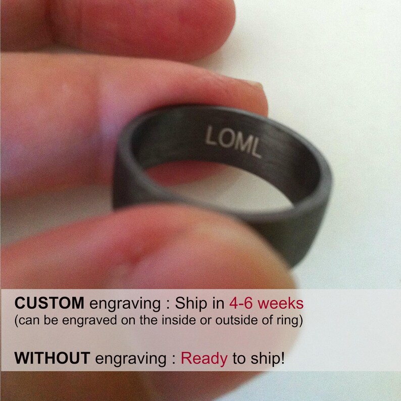 May include: A black ring with the inscription "LOML" engraved on the inside. The ring is being held by a finger.