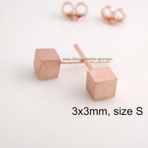 May include: A pair of small, rose gold cube earrings, each measuring 3mm x 3mm. The earrings are a simple and elegant design, perfect for everyday wear.