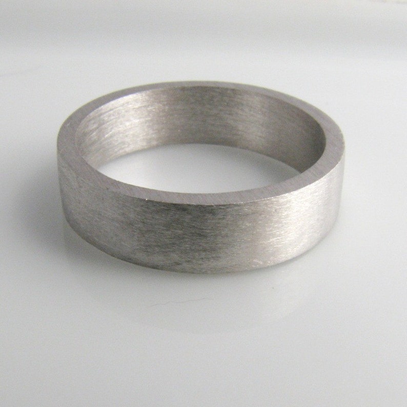 May include: A brushed silver wedding band with a flat, wide profile.