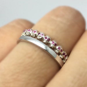 May include: A silver ring with a row of small skull charms, each with a pink gemstone in the eye sockets.