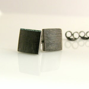 May include: A pair of brushed silver square stud earrings. The earrings are small and simple, with a brushed finish.
