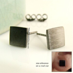 May include: A pair of black square stud earrings with a brushed metal finish. The earrings are shown on a white surface and on a model's ear for size reference.