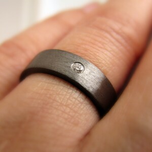 May include: A dark gray brushed metal ring with a single small diamond set in the center.
