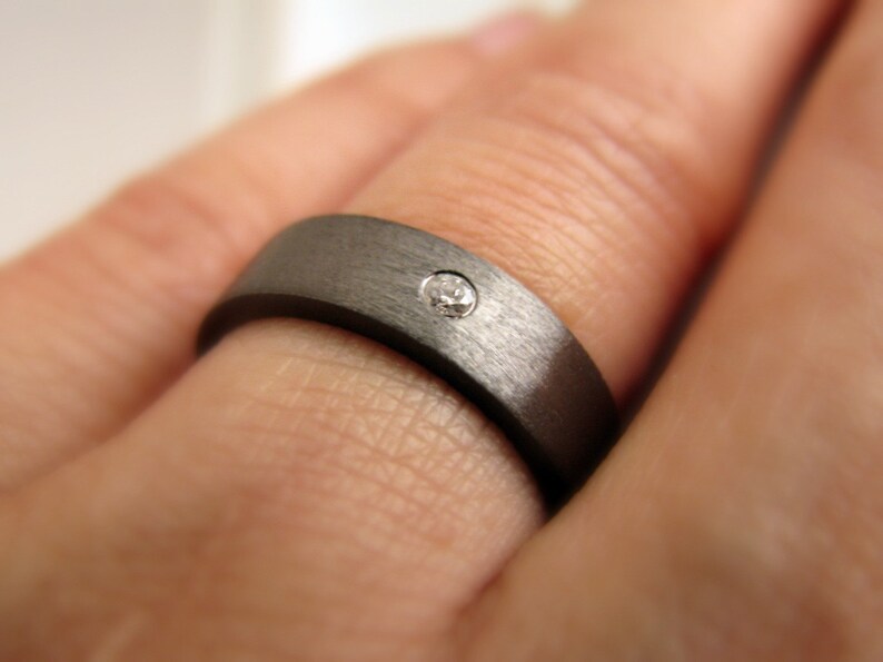 May include: A dark gray brushed metal ring with a single small diamond set in the center.