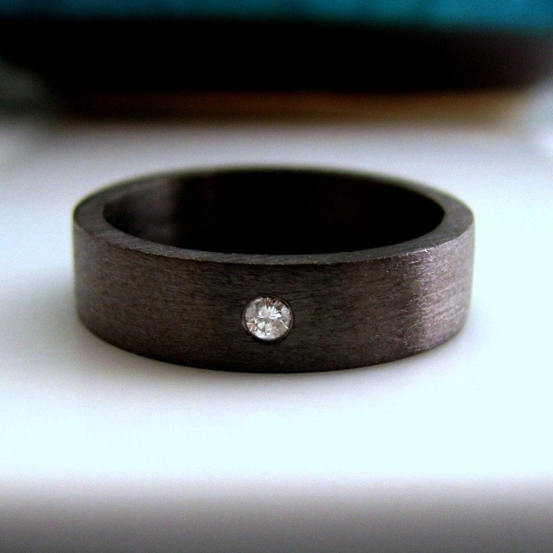 May include: A black carbon fiber ring with a single diamond set in the center.