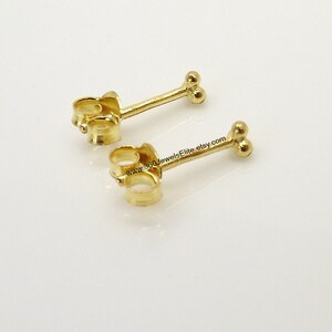 May include: A pair of gold-toned stud earrings with a double ball design. The earrings have a post and butterfly backing.