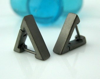 Peut inclure: Une paire de boucles d'oreilles en forme de triangle avec une finition gris foncé. Les boucles d'oreilles sont en métal et ont une fermeture à charnière.