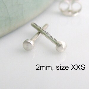 May include: Two small, silver stud earrings, each with a 2mm round top. The earrings are shown on a white surface. 2mm, size XXS