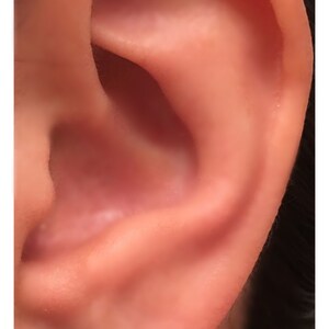 May include: A close-up of a person's ear with a small, square, dark grey earring. The earring is made of wood and has a natural, rustic look. The text "360JewelsElite.etsy.com" is visible below the earring.
