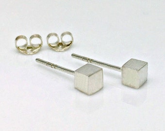 May include: A pair of silver cube stud earrings. The earrings are small and have a brushed finish.