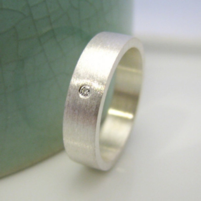 May include: A silver band with a brushed finish and a single small diamond set in the center.