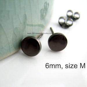 Puede incluir: Un par de pendientes de botón negros de 6 mm, talla M. Los pendientes son redondos y tienen un acabado liso y pulido.