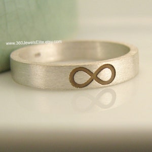 May include: A silver band ring with an infinity symbol engraved in the center. The infinity symbol is a darker color than the ring.