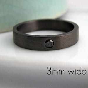 May include: A dark gray ring with a single black gemstone. The ring is 3mm wide and has a brushed metal finish. The ring is a simple, modern design.