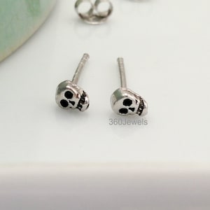 May include: A pair of silver skull stud earrings. The skulls are small and detailed, with black eyes.